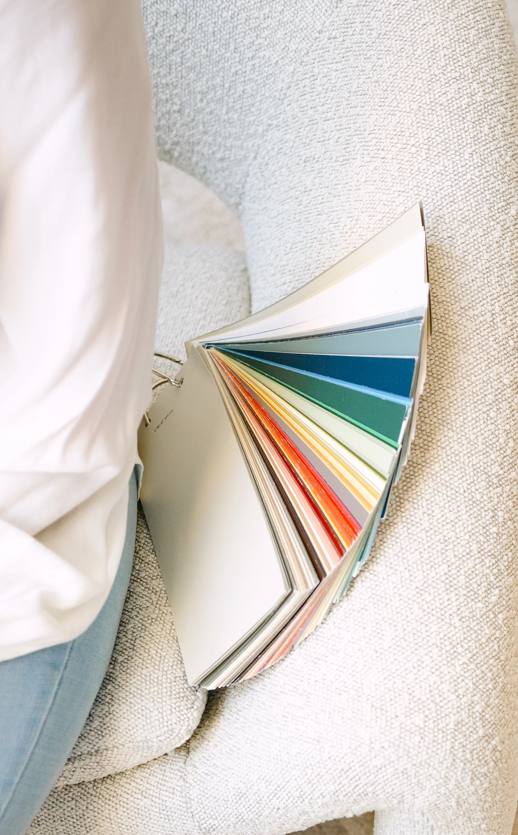 A paint color deck fanned open on a cream sofa during a design consultation